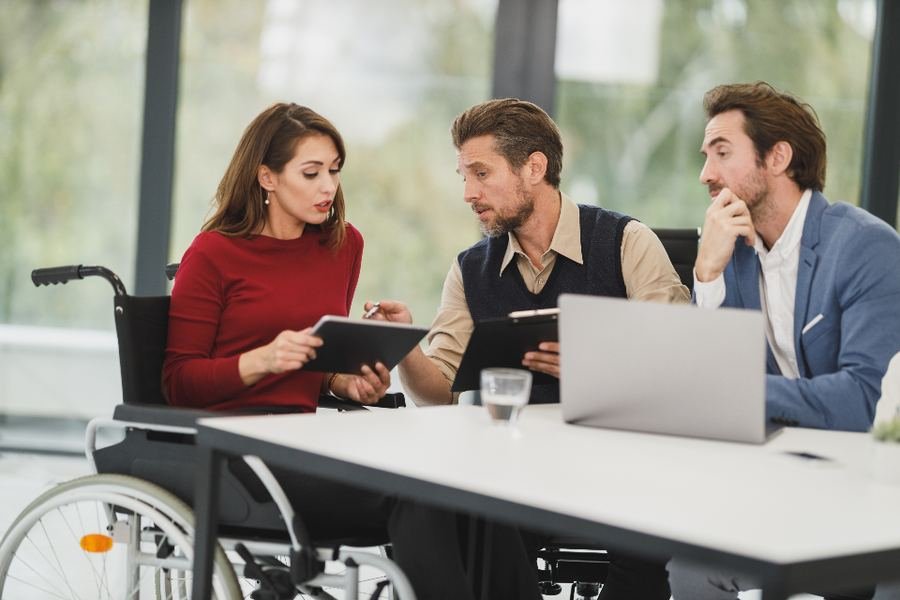 A group of colleagues in a meeting around a table, one using a wheelchair