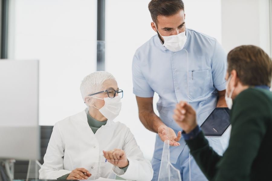 A clinical team in scrubs conferring with an older patient