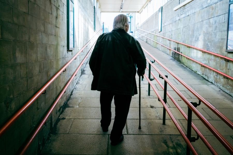 An older man walking away down a corridor with handrails