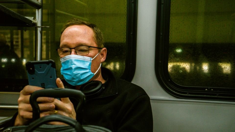 A commuter checks his phone on an early morning bus, lit by the window