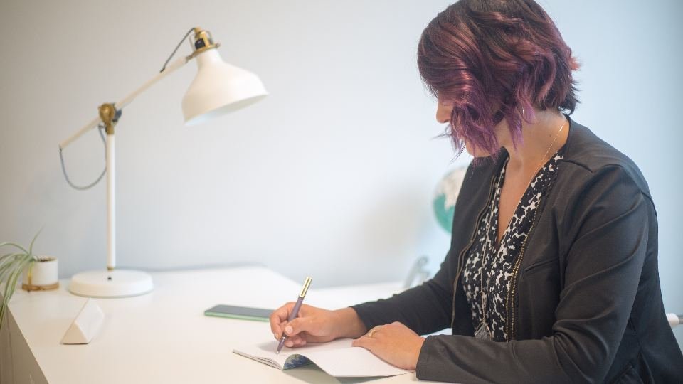 A woman writing at a desk under a warm lamp