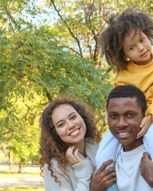 A young family together outdoors under trees