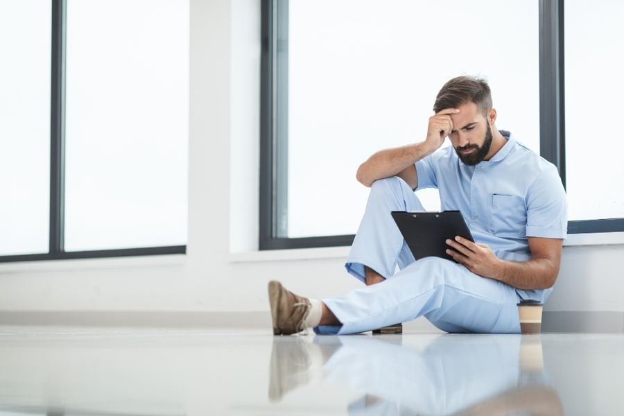A health care worker sitting on the floor by a window, taking a moment