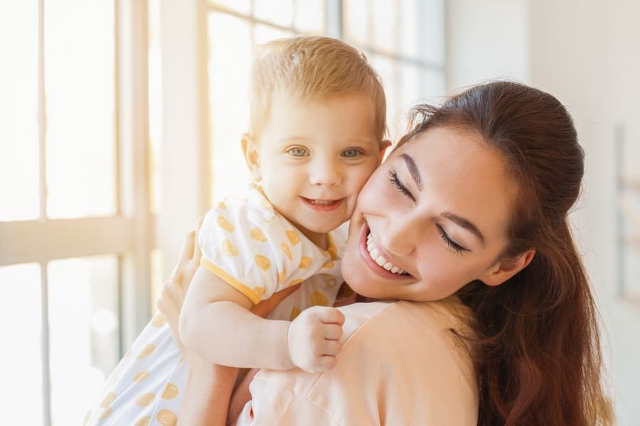A woman holding a small child by a bright window