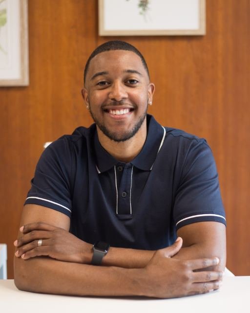 A man seated at a desk, smiling toward the camera