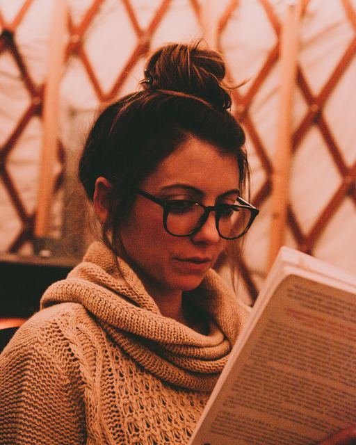 A woman in a warm scarf reading closely under soft orange light