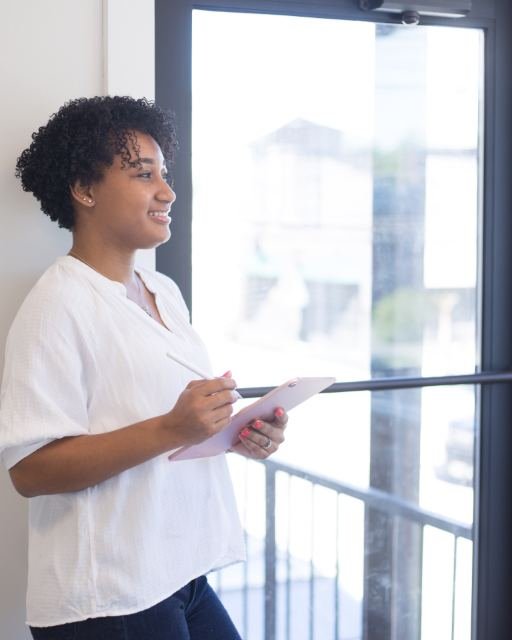 An instructor standing by a window holding a clipboard, looking out