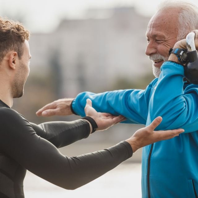 A therapist guiding an older man through a shoulder movement outdoors