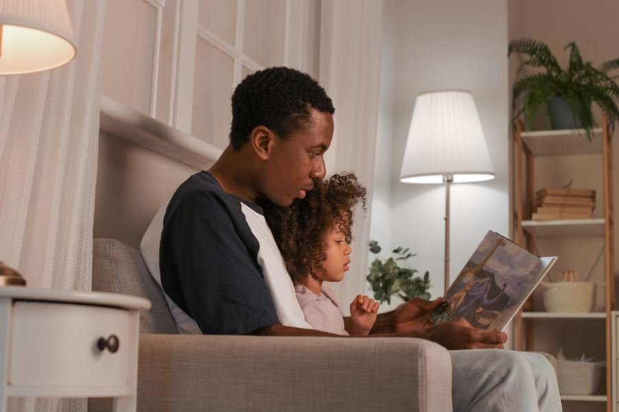 A parent and child reading together at home under a lamp